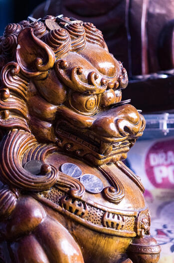 A wooden Chinese lion with coins balanced on it.